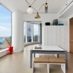 A room with a table and chairs, a bench, and a large window.