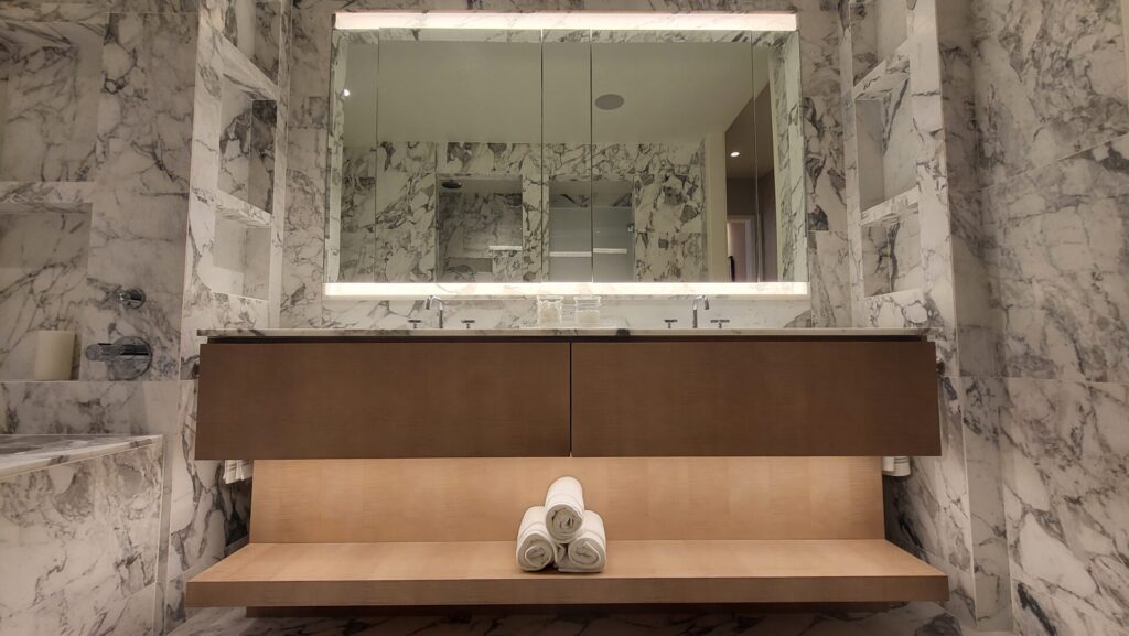 Elegant spa room with a large mirror, soft lighting, and rolled towels on a bench.
